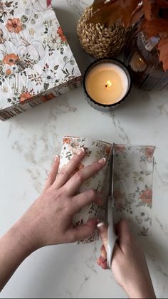 a person is cutting paper with scissors on a table next to candles and other items