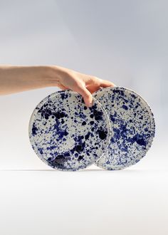 two blue and white plates being held by a person's hand on a white surface