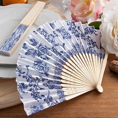 a blue and white fan sitting on top of a wooden table next to some flowers