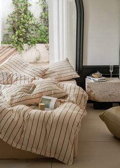 an unmade bed with striped sheets and pillows on the floor next to a mirror