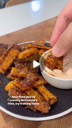 a person dipping something into a bowl on top of a plate with fried food in it