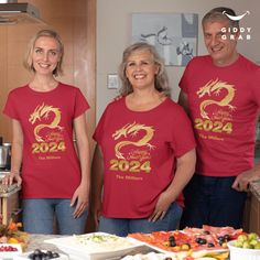 three people wearing red shirts standing in front of a table full of food