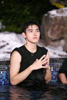 a young man sitting in the middle of a swimming pool holding his hands together and looking up