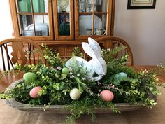 an arrangement of greenery and painted eggs on a dining room table