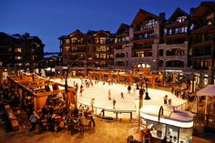 people skating on an ice rink at night in front of buildings with lit up windows