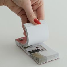 a woman's hand holding a roll of white paper with red nail polish on it