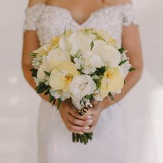 a woman holding a bouquet of white and yellow flowers on her wedding day in an off the shoulder dress