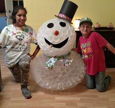 two children standing next to a snowman made out of bubble wrap and plastic cups