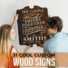 two people holding up a wooden sign that says, the couple drinks together and they are looking at each other