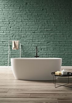 a white bath tub sitting in front of a green brick wall next to a coffee table