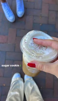 a person with red nail polish holding up a cup of iced coffee in front of their feet