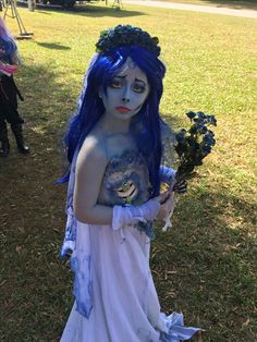 a woman with blue hair and makeup holding flowers