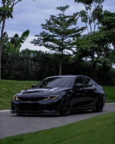 a black car parked on the side of a road next to some trees and grass