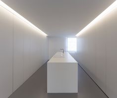 a long white counter in the middle of a room with light coming from it's windows