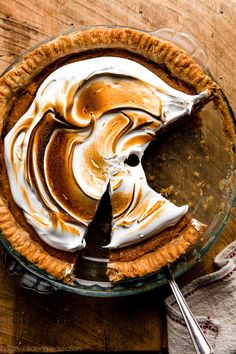 a pie with white frosting and a slice missing from it on a wooden table