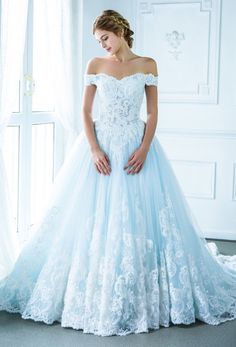 a woman in a blue wedding dress standing next to a white wall and window with her hands on her hips