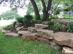 a stone wall in the middle of a grassy area next to a tree and lawn