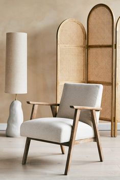 a white chair sitting next to a lamp on top of a hard wood floor covered in wicker