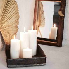 some white candles are sitting on a tray in front of a mirror and an umbrella