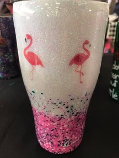 a pink and white cup with two flamingos painted on it's sides sitting on a table