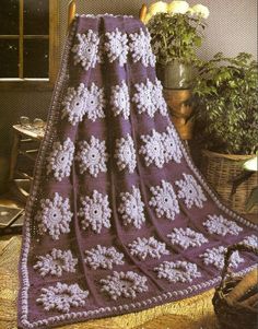 a purple crocheted blanket sitting on top of a wooden chair next to a potted plant