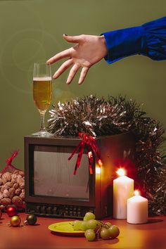 a person reaching for a glass of wine in front of a television set with christmas decorations and candles