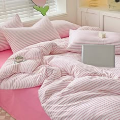 a bed with pink and white striped comforter next to a laptop on a desk