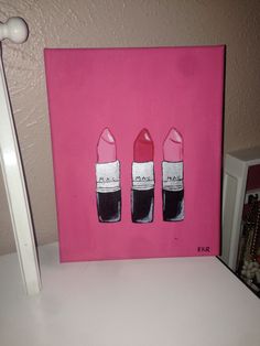 three lipsticks are painted on a pink canvas with white trim and one is black, the other is red