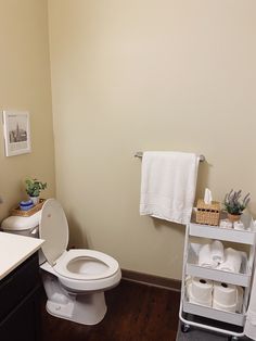 a white toilet sitting in a bathroom next to a sink and towel rack with towels on it