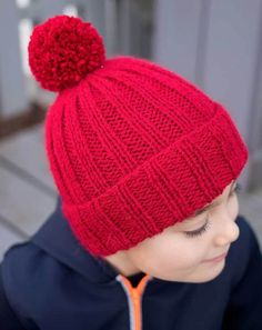 a young boy wearing a red knitted hat with a pom - pom