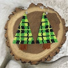 a pair of green and black beaded christmas tree earrings sitting on top of a piece of wood