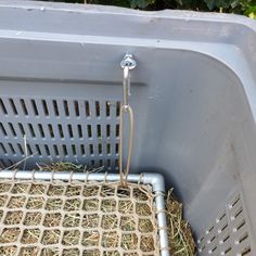 a gray trash can filled with hay and straw next to a wire basket on the ground