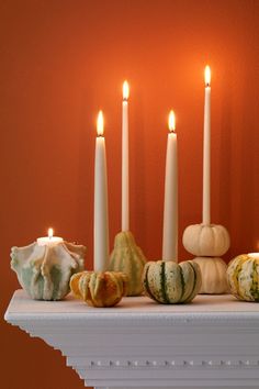 a mantle with candles and gourds on it in front of an orange wall