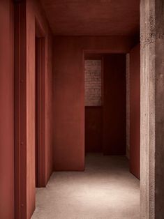 an empty hallway with red walls and concrete pillars in the center, leading to another room