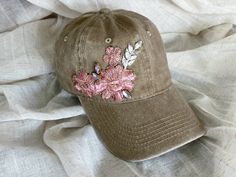 a brown hat with pink flowers on it sitting on a white cloth covered bed sheet