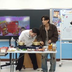 two people standing over a table with food on it