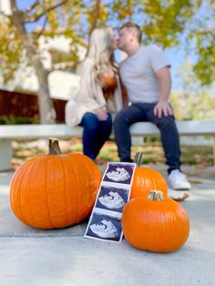 a man and woman sitting on a bench next to two pumpkins with pictures in them