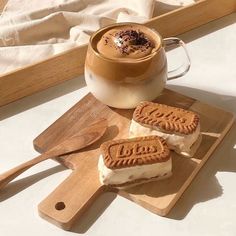 two cookies are on a cutting board next to a cup of hot chocolate and a spoon