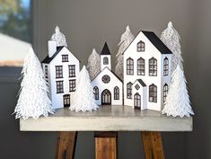 three white paper houses on top of a wooden table with trees in the front and behind them