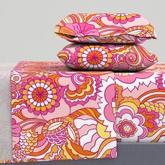 three pillows are stacked on top of each other in front of a gray wall with pink and orange designs