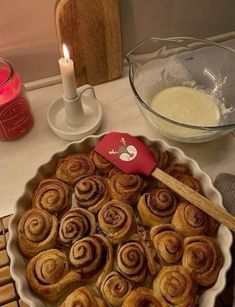 cinnamon rolls in a pie pan on a table with candles and other baking supplies around it