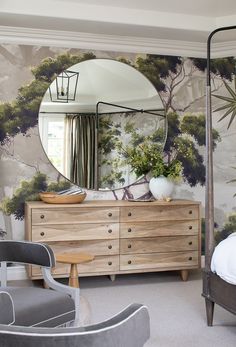 a bedroom scene with focus on the dresser and large round mirror over the headboard