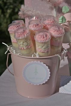 a pink bucket filled with cupcakes on top of a table next to a tree