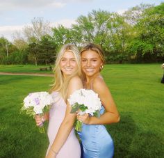 two beautiful young women standing next to each other on a lush green field with trees in the background