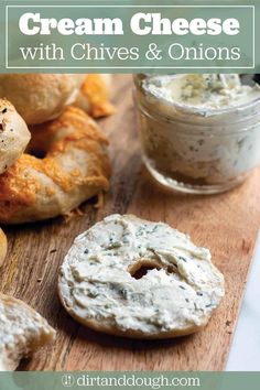 cream cheese with chives and onions on a wooden cutting board next to bagels