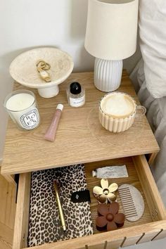 an open drawer on a bed with makeup and other items in it next to a lamp