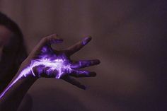 a person's hand with purple and black paint on it, in front of a dark background