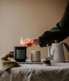 a person holding a lit candle on top of a table next to a tea pot