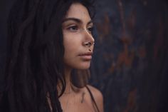 a woman with long black hair and piercings on her nose looking off to the side