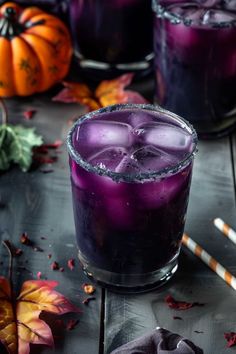 two glasses filled with purple liquid sitting on top of a table next to pumpkins